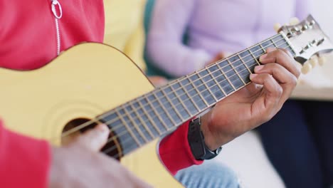 Midsection-of-african-american-man-playing-guitar-with-friends-at-home,-in-slow-motion