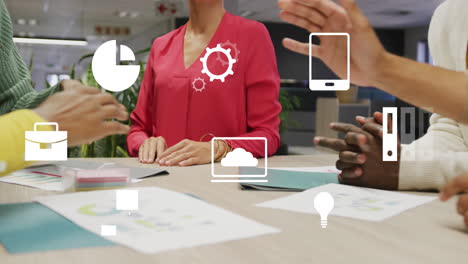 Animation of digital icons over mid section of colleagues stacking their hands together at office