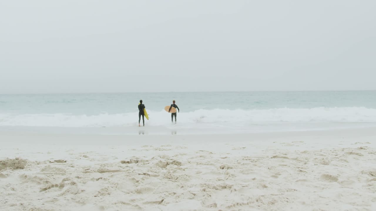해변 4k에서 서프보드와 함께 달리는 두 남성 서퍼의 뒷면