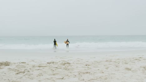 rear view of two male surfers running together with surfboard on the beach 4k