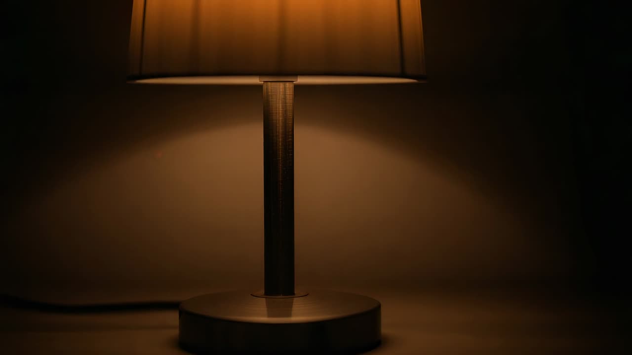 Telecamera che si muove verso l'alto rivelando una lampada da tavolo su un tavolo accanto a una parete semplice, mostrando paralume, fusto e cavo di alimentazione