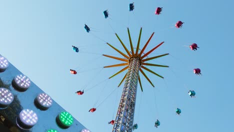 amusement park scenery, colorful lights flickering in foreground with gigantic vertical chain fair swing in background, clear blue sky, static low angle, day