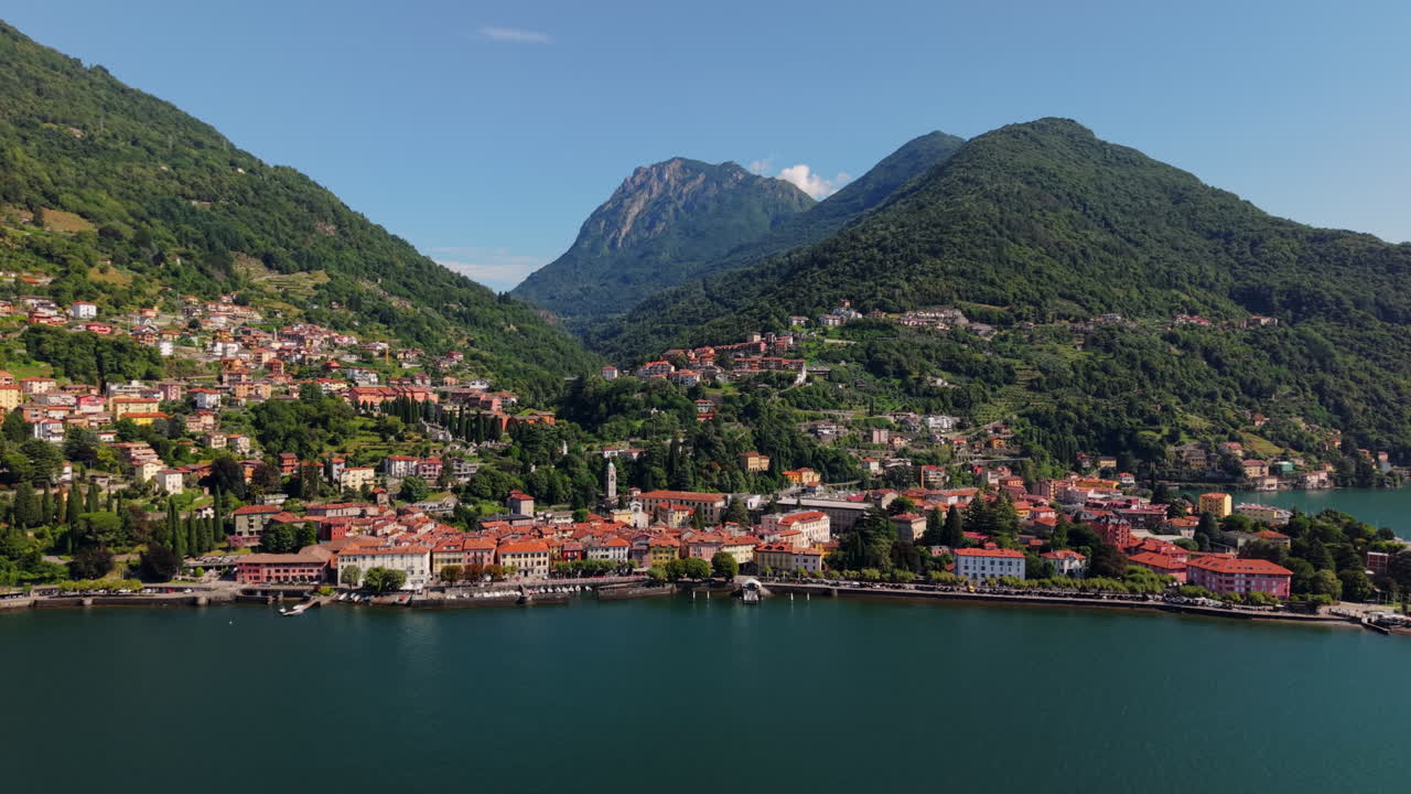 Drone retreats from the lakeside, revealing the colorful town and surrounding mountains on Lake Como in Italy