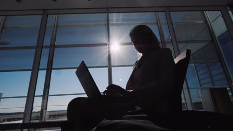 Silhouette-Einer-Geschäftsfrau-Mit-Einem-Laptop,-Der-In-Erwartung-Ihres-Fluges-Arbeitet,-Sitzt-Im-Großen-und-Ganzen