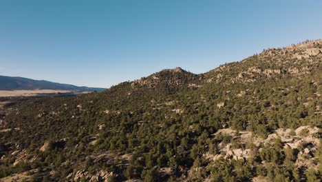 drone flying over midland hill in colorado with mountains in the background and trees in foreground