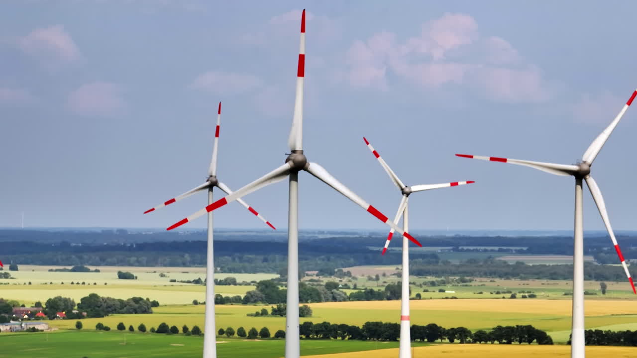 Telephoto drone shot circling wind turbines rotating in sync, sunny summer day