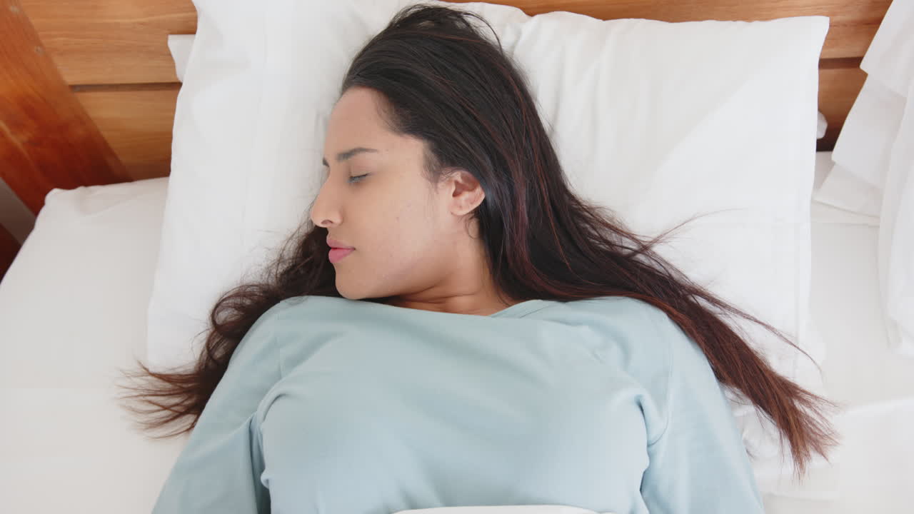 Lying in bed, asian woman massaging temples and relaxing with eyes closed, at home
