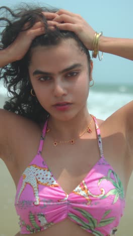 confident young woman on beach, hands in hair, wearing a pink bikini top