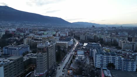 Sofia-Bulgaria-skyline-buildings-at-sunset,-road-through-cityscape,-Drone-shot