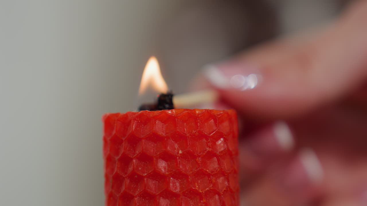 primer plano extremo de una vela roja encendida con un fósforo por una persona con uñas cuidadosamente cuidadas, el suave resplandor de la llama mejora la atmósfera cálida y acogedora