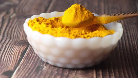 polvo de cúrcuma en un cuenco blanco con cuchara de madera
