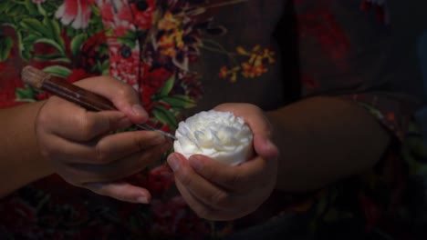un primer plano de una mano de mujer tallando una barra de jabón en una flor con un cuchillo