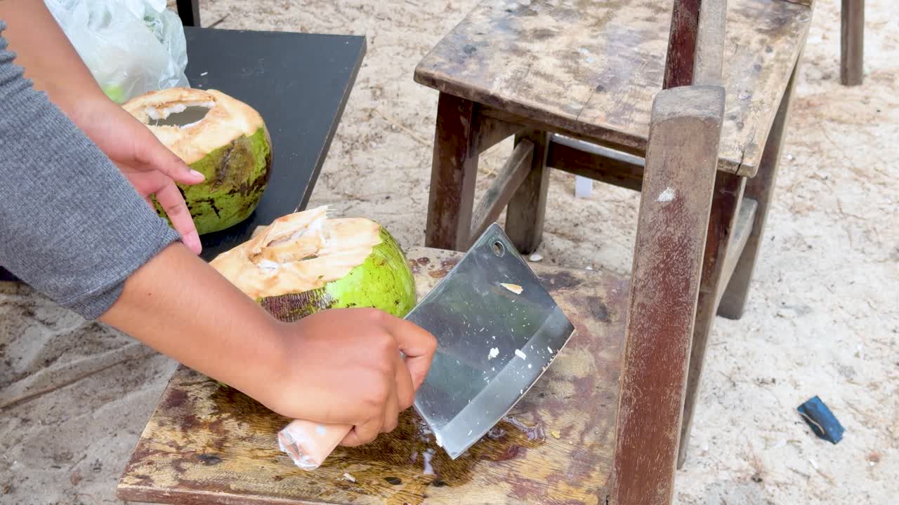 Un venditore usa una grande mannaia di metallo per aprire una noce di cocco verde fresca all'aperto.