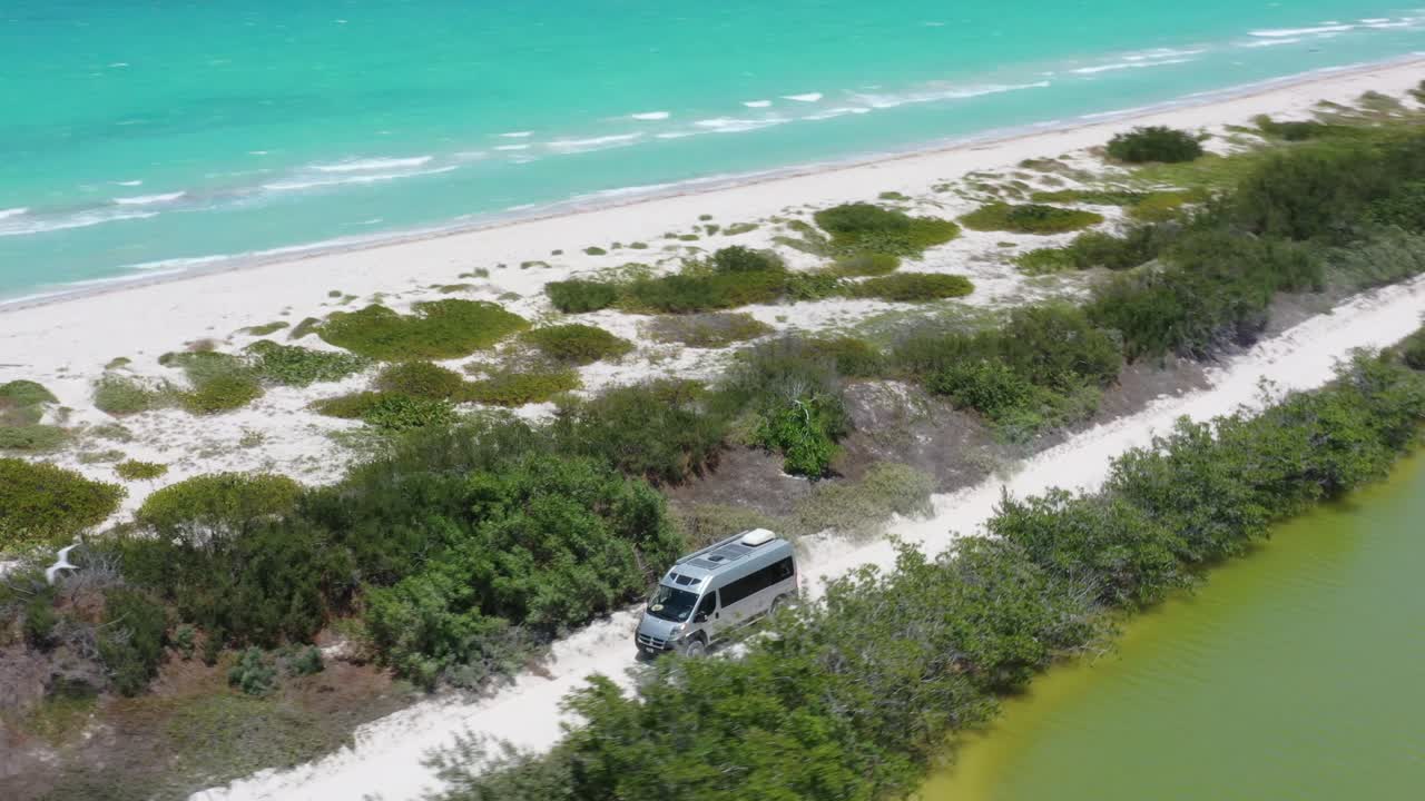 Grey Van driving off road with Caribbean ocean and salt lake view. Mexico, Rio Lagartos, aerial drone shot.