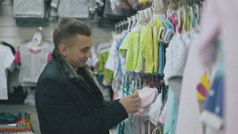 happy handsome man takes small pink baby hat in store