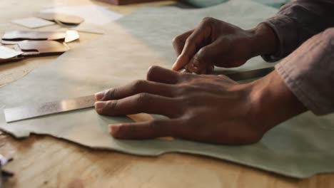 close up of hands of african american craftsman cutting leather precisely in leather workshop