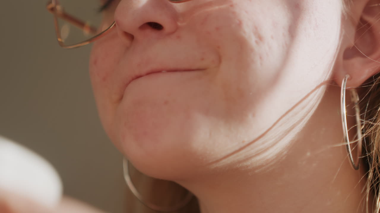 Donna bianca che sorride dopo un sorso, primo piano di donna caucasica con occhiali e lentiggini, sorriso gioioso e fossette, tazza di ceramica messa da parte, risata spontanea, bagliore caldo e cinematografico, atmosfera di conversazione in cucina.