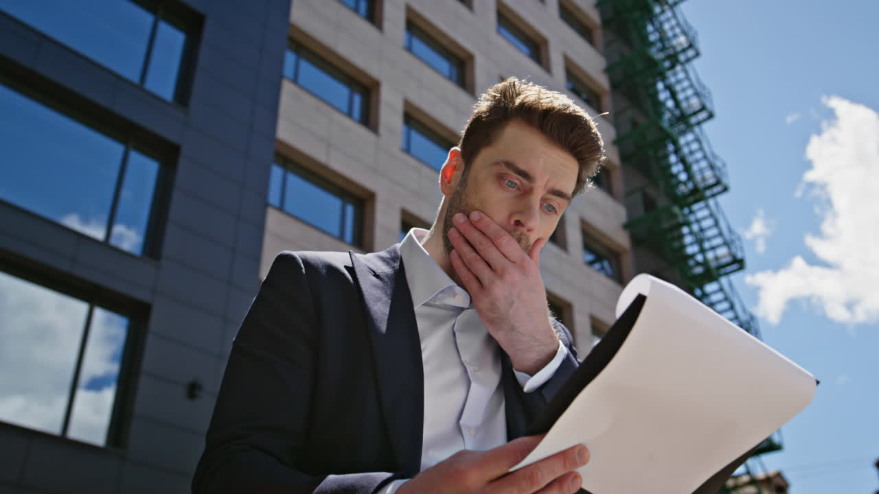 Worried professional reading paperwork standing near office building closeup