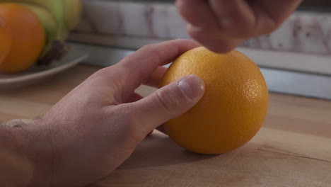 man's hand cut orange fruit with knife on wooden chopping board