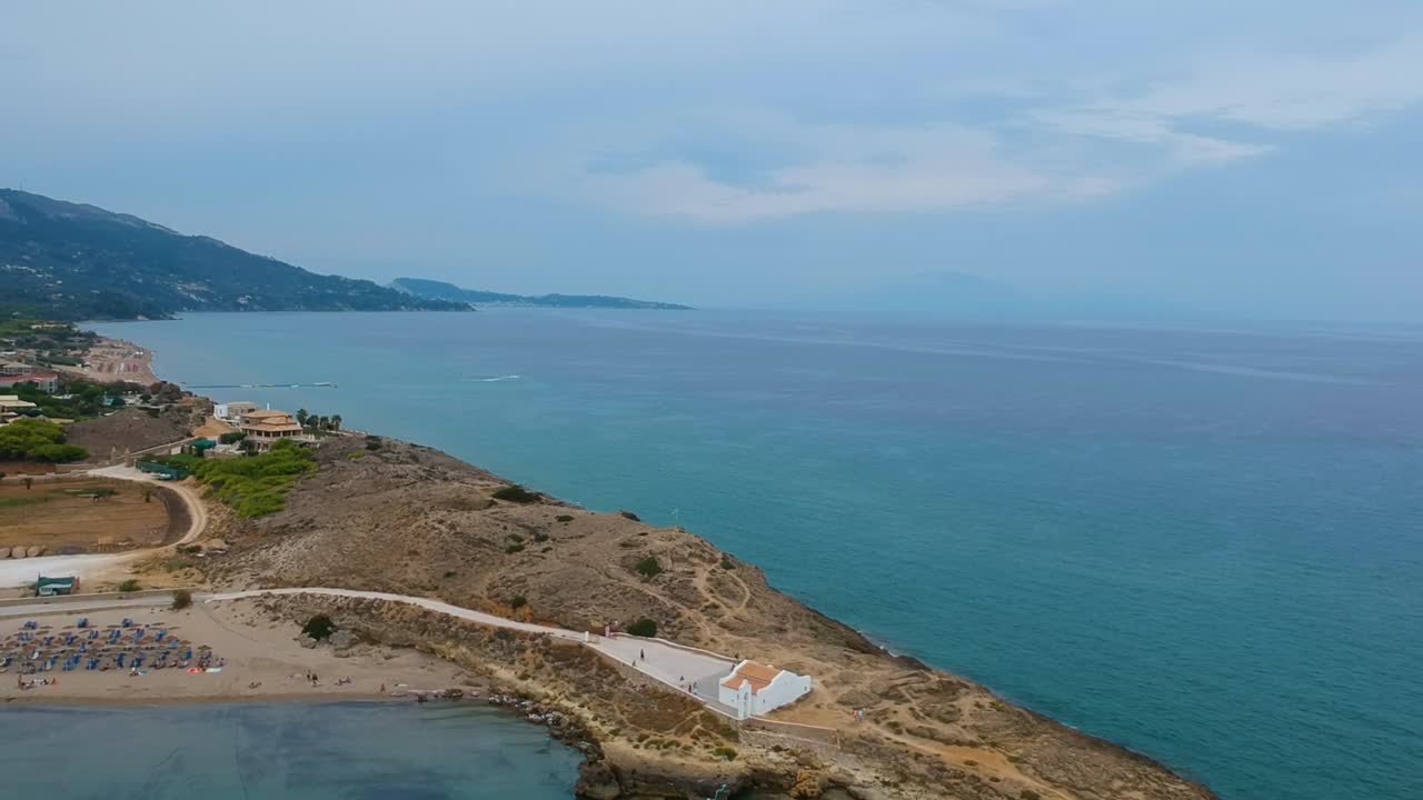 Zakynthos Island Greece Point St. Nicholas beach and rocky cliffs with St. Nikolaos church visible center, Aerial drone dolly-in reveal shot