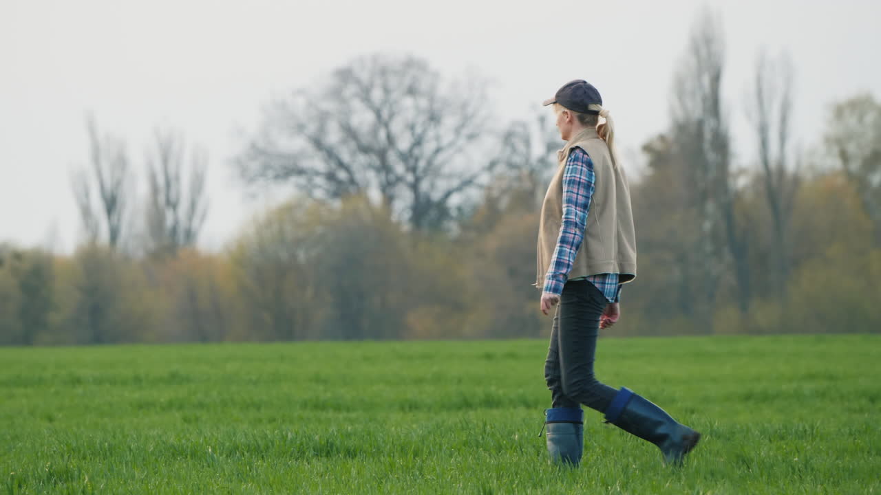 여자 농부는 겨울밀이 돋아난 그녀의 밭으로 간다