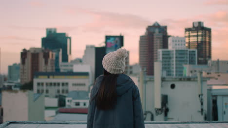 happy young woman on rooftop with arms raised celebrating freedom enjoying independent lifestyle looking at beautiful view of city skyline at sunset