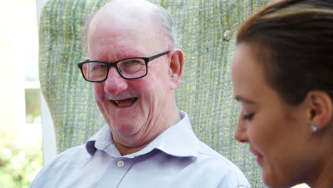 Senior-Man-Sitting-In-Chair-And-Talking-With-Nurse-In-Retirement-Home