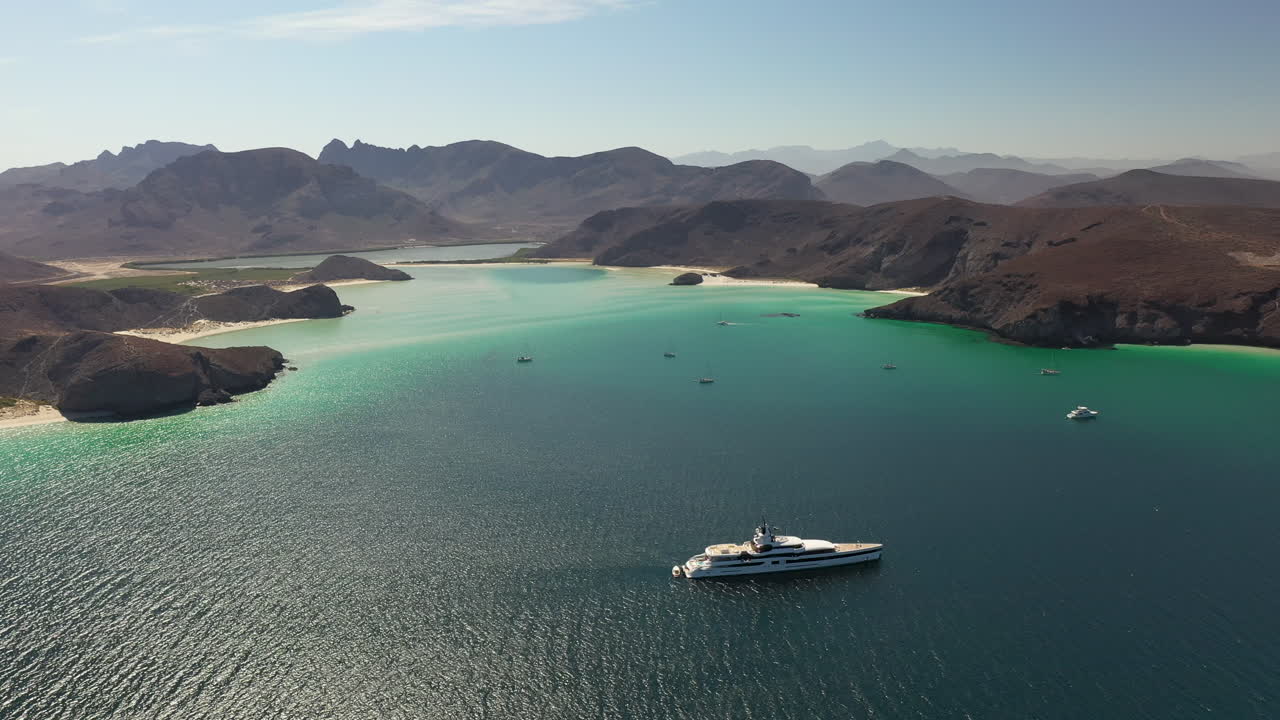 발란드라 해변, 붉은 언덕, 청록색 바다, 백사장 해변, 만에 요트가 있는 산의 전망을 영화처럼 넓게 회전하는 드론 샷