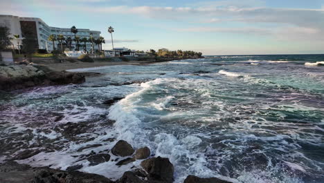 waves crashing on the shore near a coastal hotel