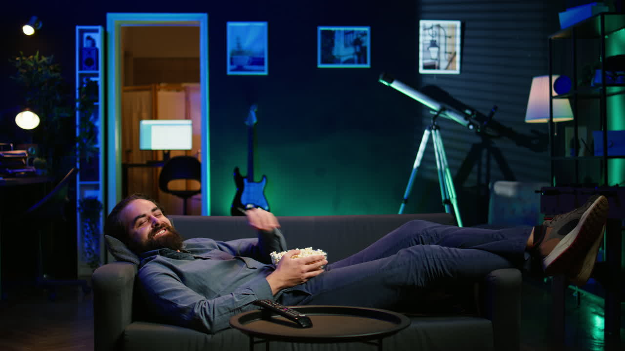 재는 남자 는 소파 에 누워서 팝콘 을 먹으면서 재는 코미디 영화 를 보고 웃고 있다