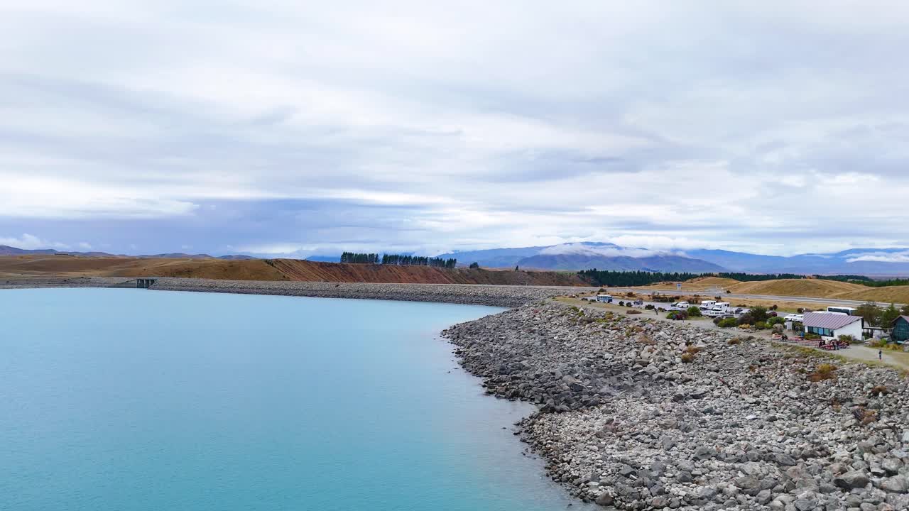 Aerial footage captures Lake Pukaki's turquoise waters and rocky shoreline under a cloudy sky, showcasing New Zealand's natural beauty