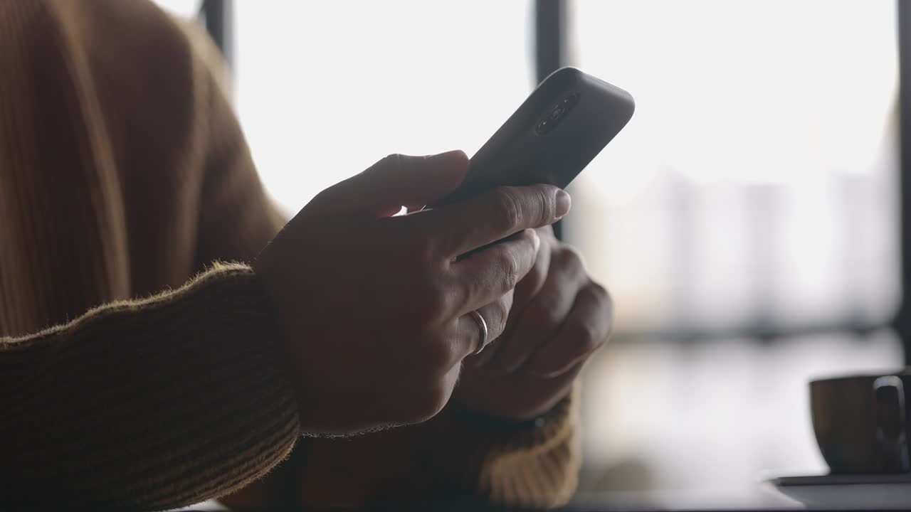 vista lateral de las manos del hombre con el reloj usando el teléfono móvil mientras trabaja en la computadora portátil. dedos masculinos escribiendo y tocando en el teléfono inteligente. mensajes de texto y desplazamiento. cámara lenta.