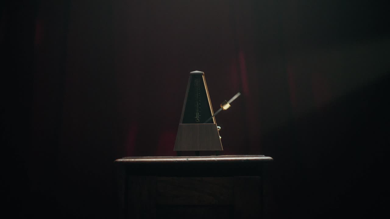 A close-up shot of a classic mechanical metronome ticking on a dark wooden surface. The camera performs a smooth dolly-in move toward the swinging pendulum, followed by a dolly-out. Moody red lighting
