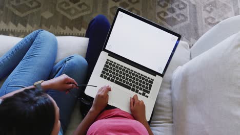 Biracial-sisters-sitting-on-sofa-and-using-laptop-with-copy-space,-in-slow-motion