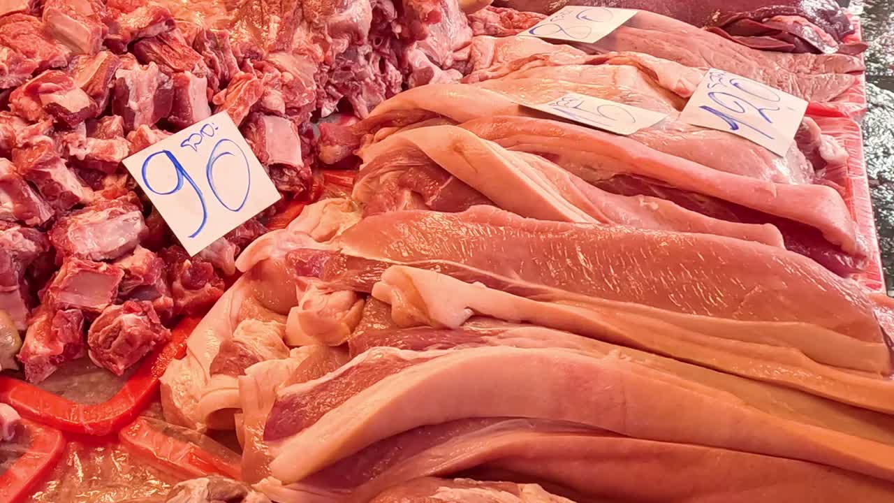 A butcher's hand carefully organizes raw pork belly slices and meat cuts at a market