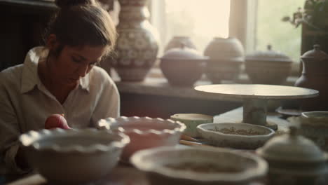 focused artist making picture on pot in pottery. woman decorating clay product