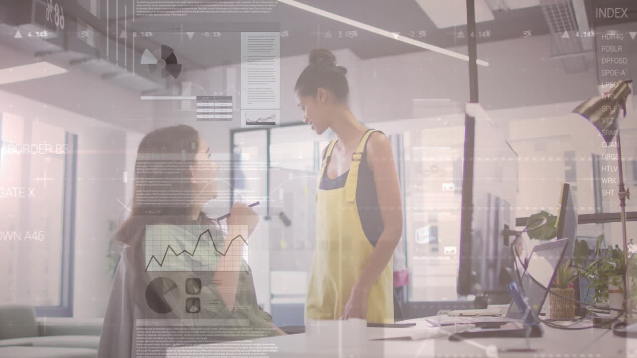 Standing woman in overalls pointing at screen guiding coworker to board eliciting nod in office