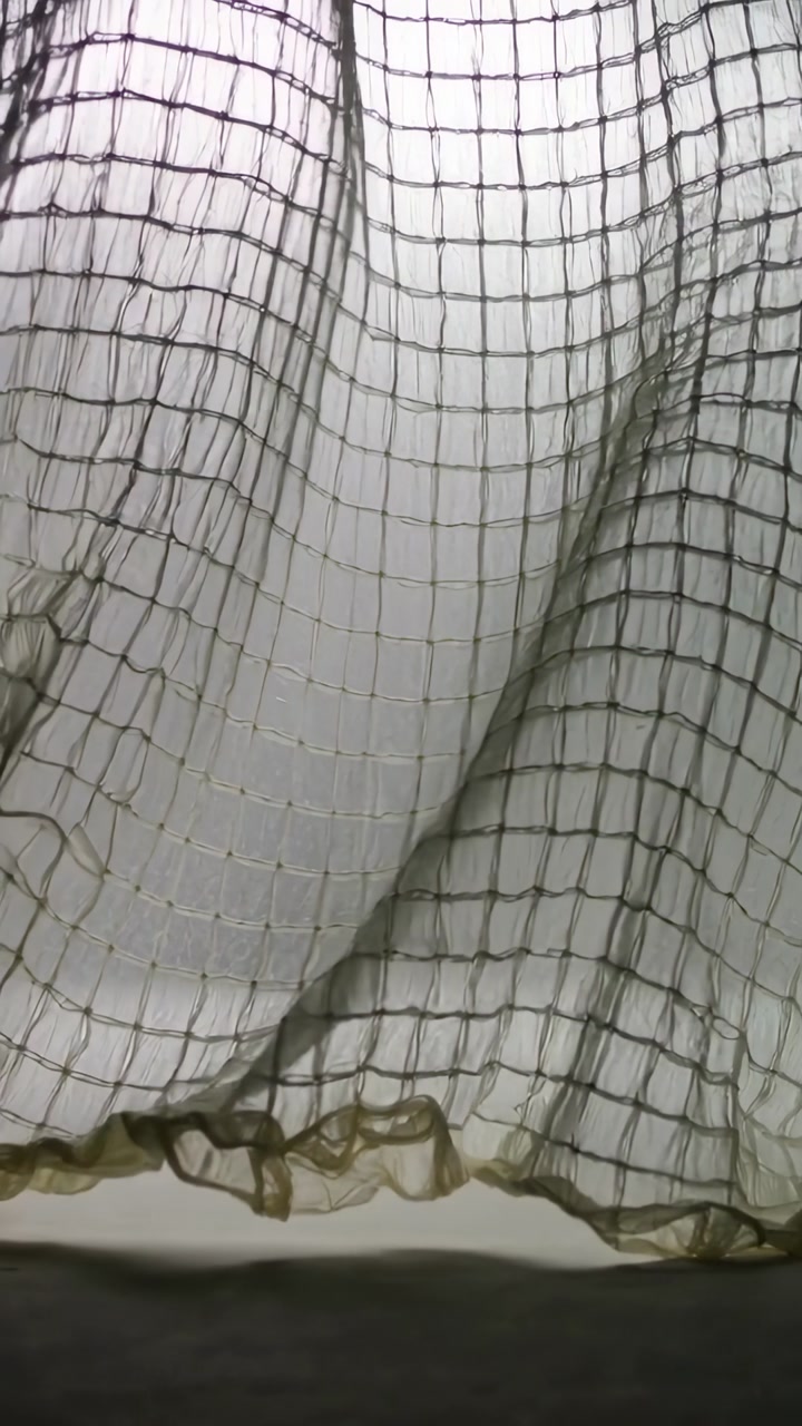 Vertical video: Shifting sheer grid curtain moving from draft at window with ruffle hem and sill