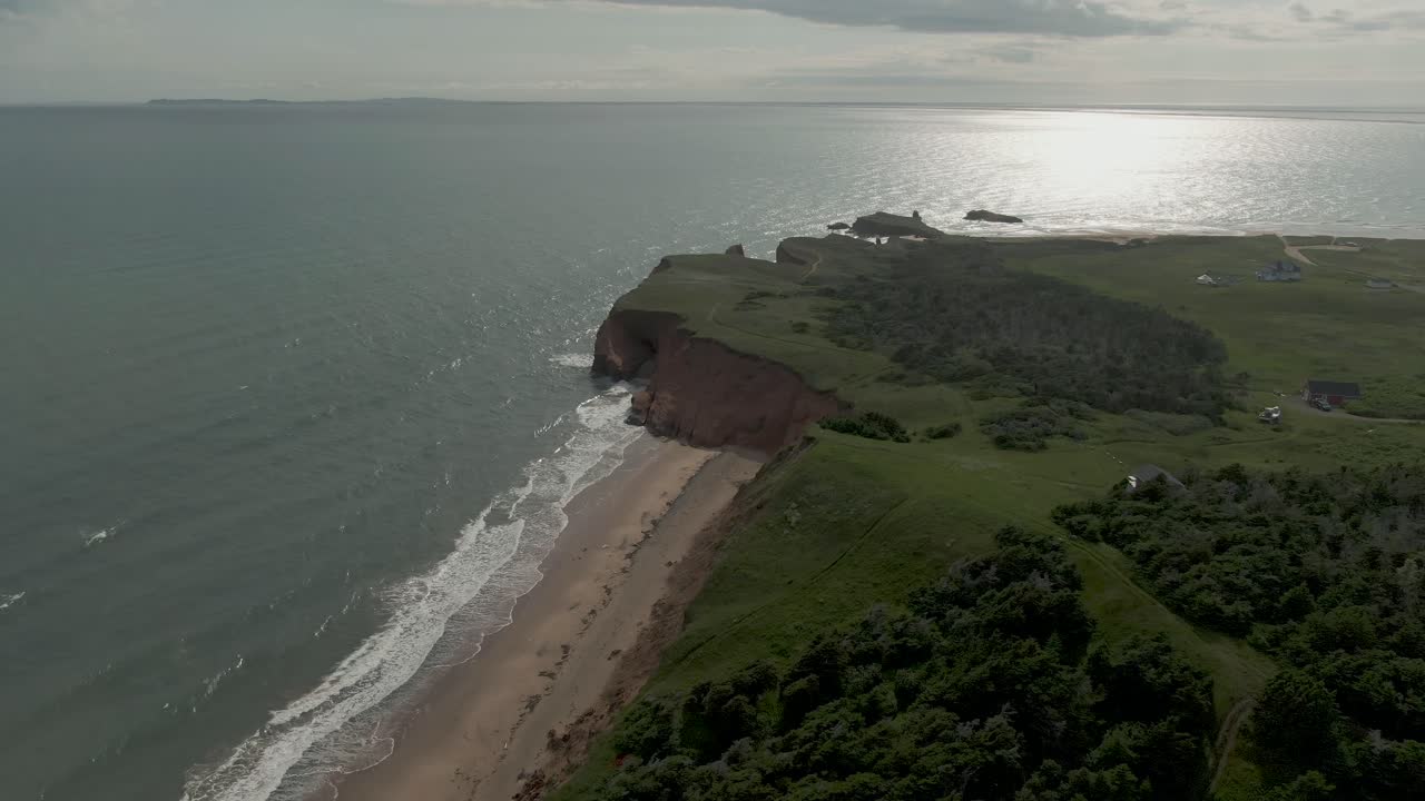 la inclinación aérea revela una toma de llanuras verdes y olas rompiendo en la playa de la isla de quebec