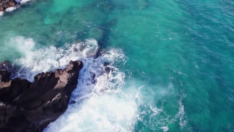 drone-shot-looking-down-into-the-clear-turquoise-water-off-the-coast-of-Oahu-Hawaii-as-the-waves-crash-onto-the-peninsula-formed-by-volcanos