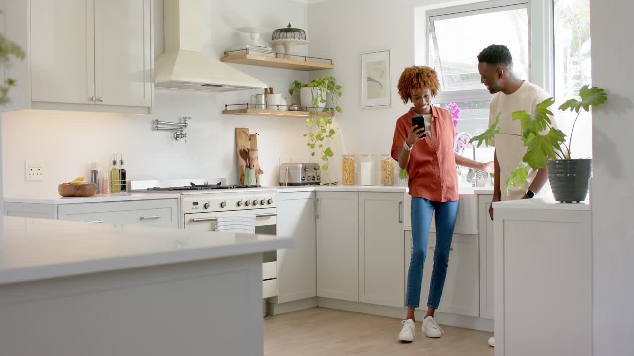 African American couple scrolling and showing phone clip, dancing and mimicking at sink, copy space