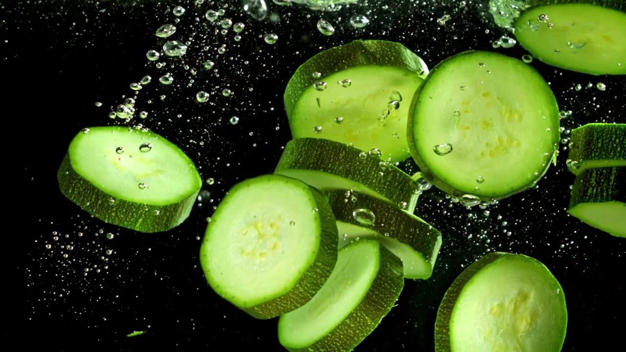 Fette fresche di zucchine verdi e cetrioli che galleggiano in acqua con bolle.