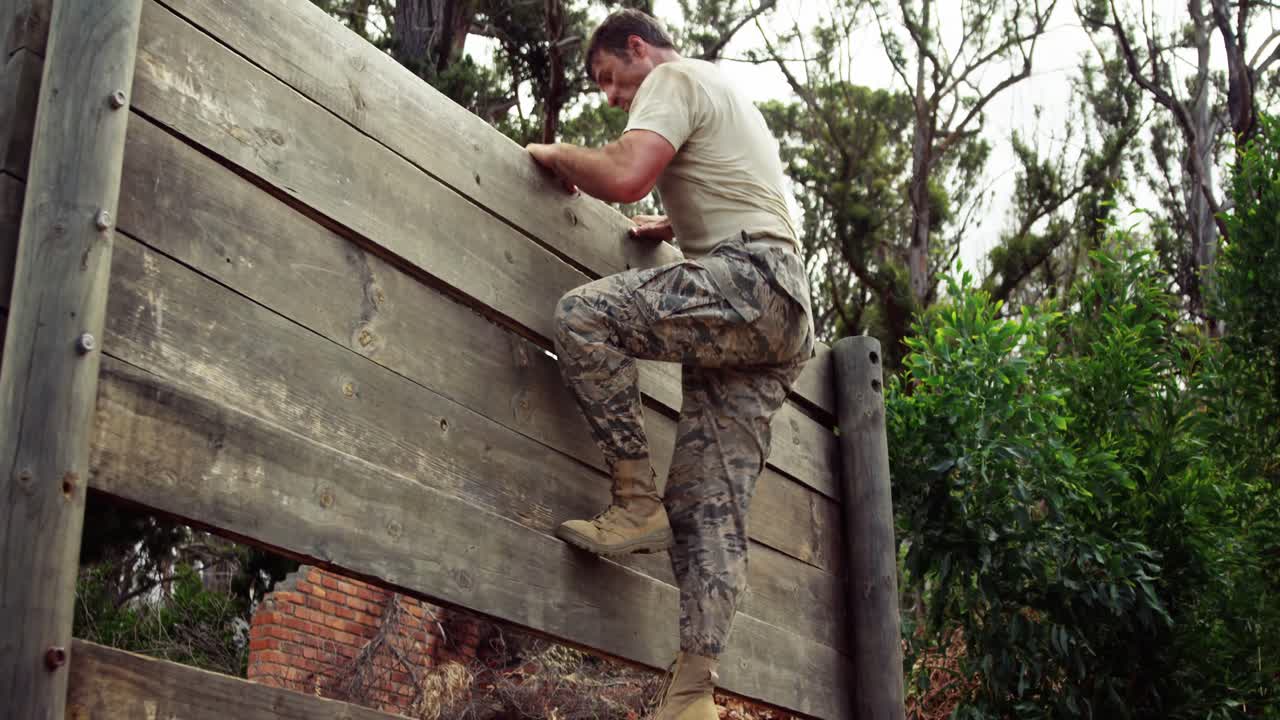 Soldato militare che si arrampica su un muro di legno al campo di addestramento 4k