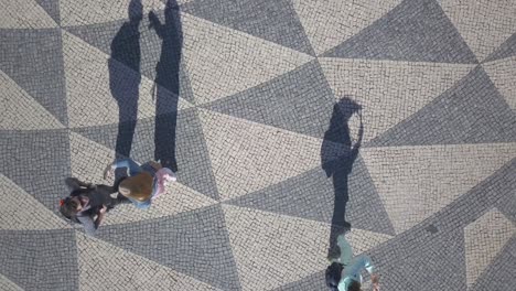 people speaking and photographing cityscape from cobblestones pavement using cell phone in lisbon, portugal