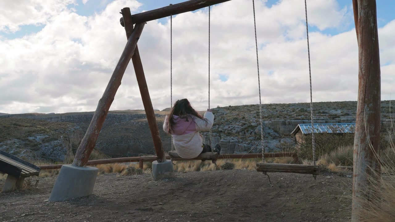 Giovane donna che si gode un'altalena rustica con un paesaggio montano sotto cieli nuvolosi e drammatici in Argentina.