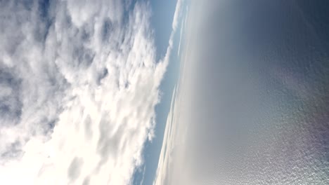 cinematic vertical aerial view of the sea with many reflections between the clouds and the sky