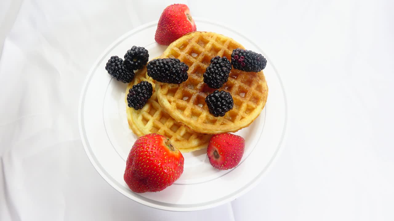 A vibrant breakfast scene featuring fresh strawberries and blackberries paired with warm golden waffles