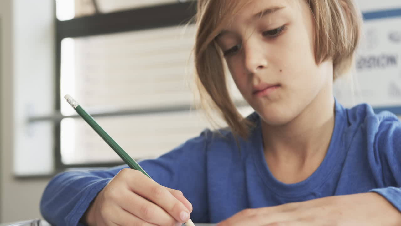 In school, focused student writing with pencil in classroom, concentrating on task