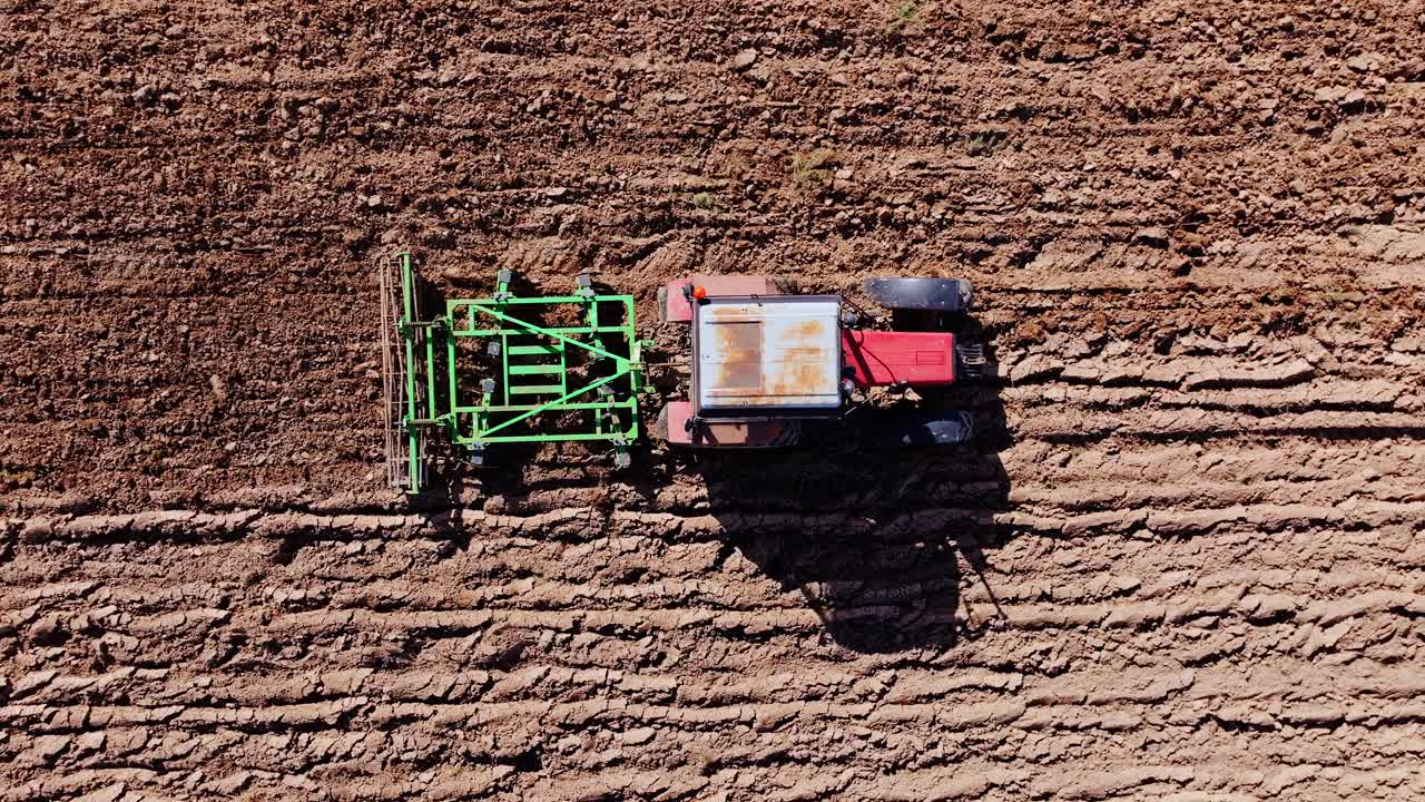Cinematic top view of tractor tilling textured earth in warm European spring sun