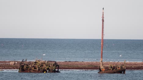 cinematic view of the ss kaffir shipwreck off ayr, scotland. rusted hull and mast sit in shallow waters, offering a haunting glimpse of maritime history and coastal decay